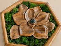 Close-up of the hand-carved walnut magnolia, showing broad sculpted petals, natural wood grain, preserved moss and a green glass cabochon.