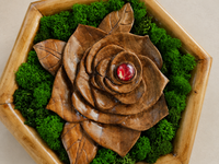 Close-up of the hand-carved walnut rose, showing its layered petals, natural wood grain, preserved moss and red glass cabochon.