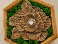 Close-up of the hand-carved walnut camellia, showing its layered petals, radial carving, preserved moss and pale glass cabochon.