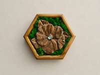 Front view of Mini Botanical Violet, a hand-carved Japanese acacia flower with preserved moss, a blue-green glass cabochon and a pine frame.
