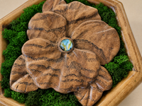 Close-up of the hand-carved Japanese acacia violet, showing its sculpted petals, dark natural grain and blue-green glass cabochon.