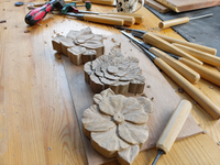 Three unfinished Mini Botanical flower carvings on a workshop bench among woodcarving chisels, pencil marks, wood chips and shavings.