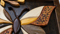 Close-up craftsmanship detail showing carved wood, relief intarsia, natural grain and hand-finished botanical elements.